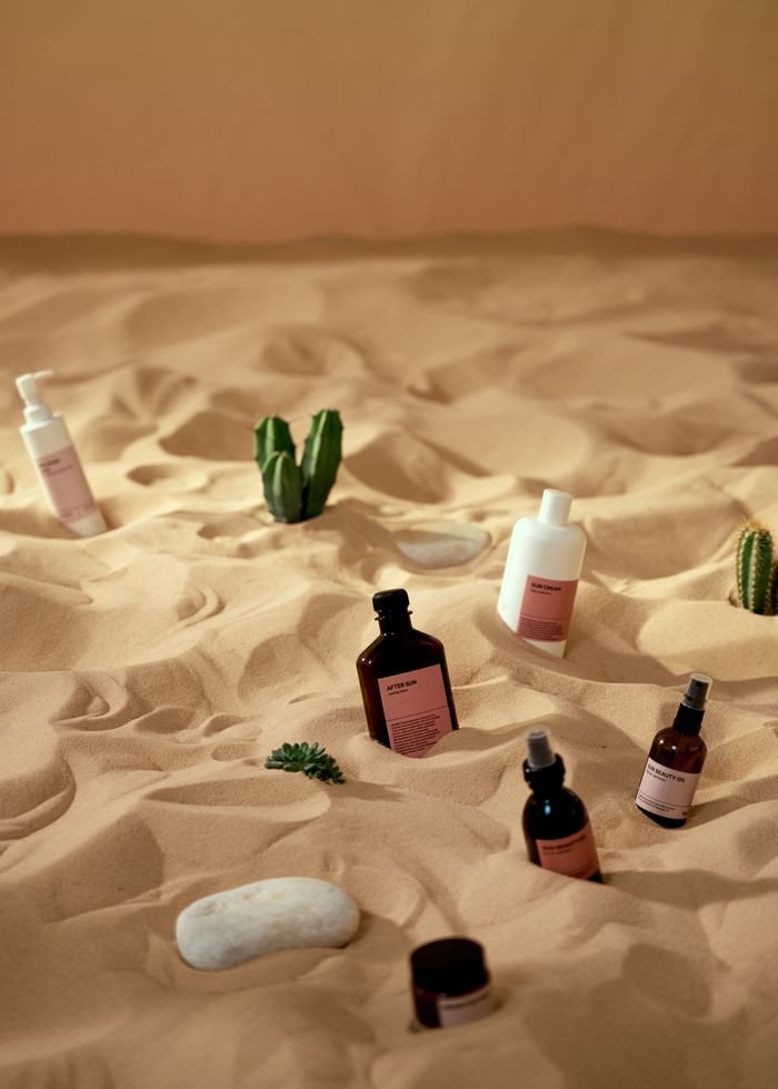 Skincare products artfully displayed on sand with a desert theme.